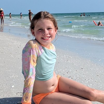 Olivia sitting on a white-sand beach